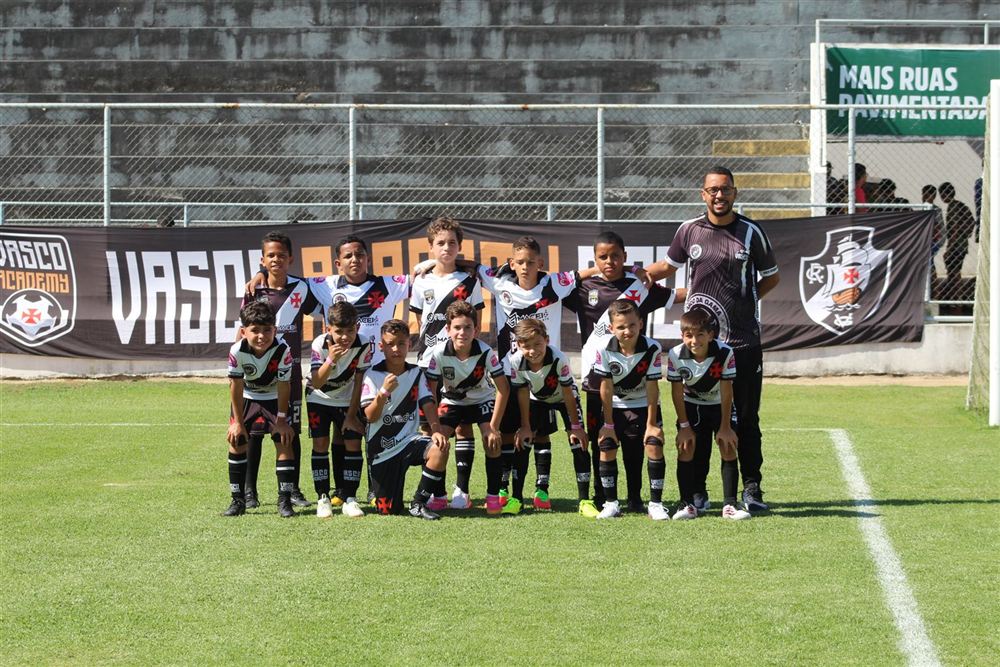 Elenco posado com o professor em frente à faixa da Vasco Academy